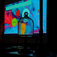 A glass dome on a stand in front of a projection screen. The dome is transparent and allows the projection screen to be seen from the inside. The screen shows a presentation with the title "The Benefits of Making Science Accessible."